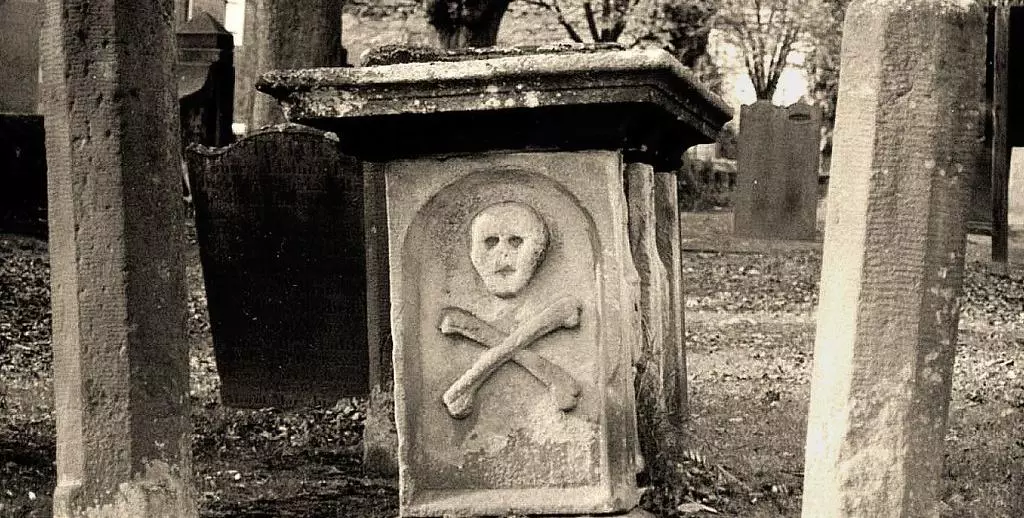 Sepia photo of skull and cross bones on a grave in Eyam Village church