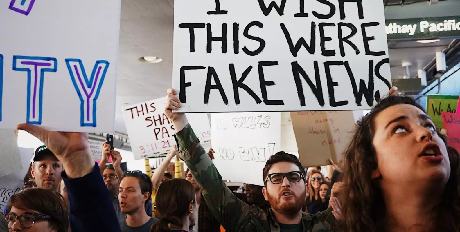 Protest with a man holding a placard that says 'I wish this were fake news'