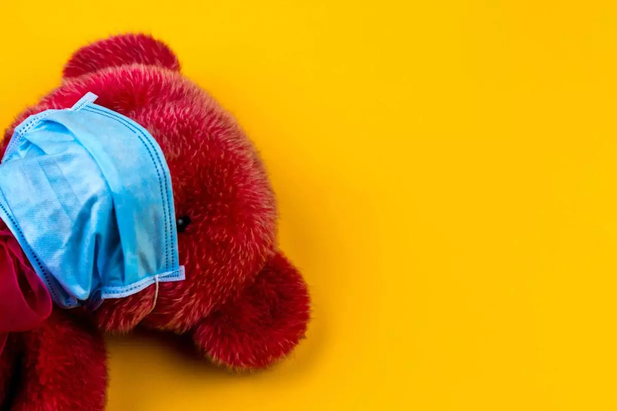 Red teddy bear wearing a blue facemask on a yellow background